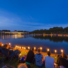 Menschen sitzen mit Picknickdecken um den Hollersee und lauschen einem klassischen Konzert 